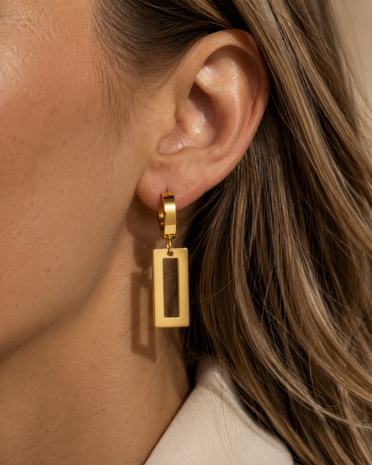 18K gold plated lange vierkante oorbellen gedragen door een model. Elegante gouden hangoorbellen met een moderne en stijlvolle uitstraling.