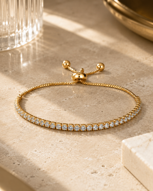 18K gold plated tennis armband met zirkonia liggend op een luxe travertin tafel in warm daglicht. Elegante lifestylefoto met verfijnde styling en premium uitstraling voor een exclusieve sieradencollectie.