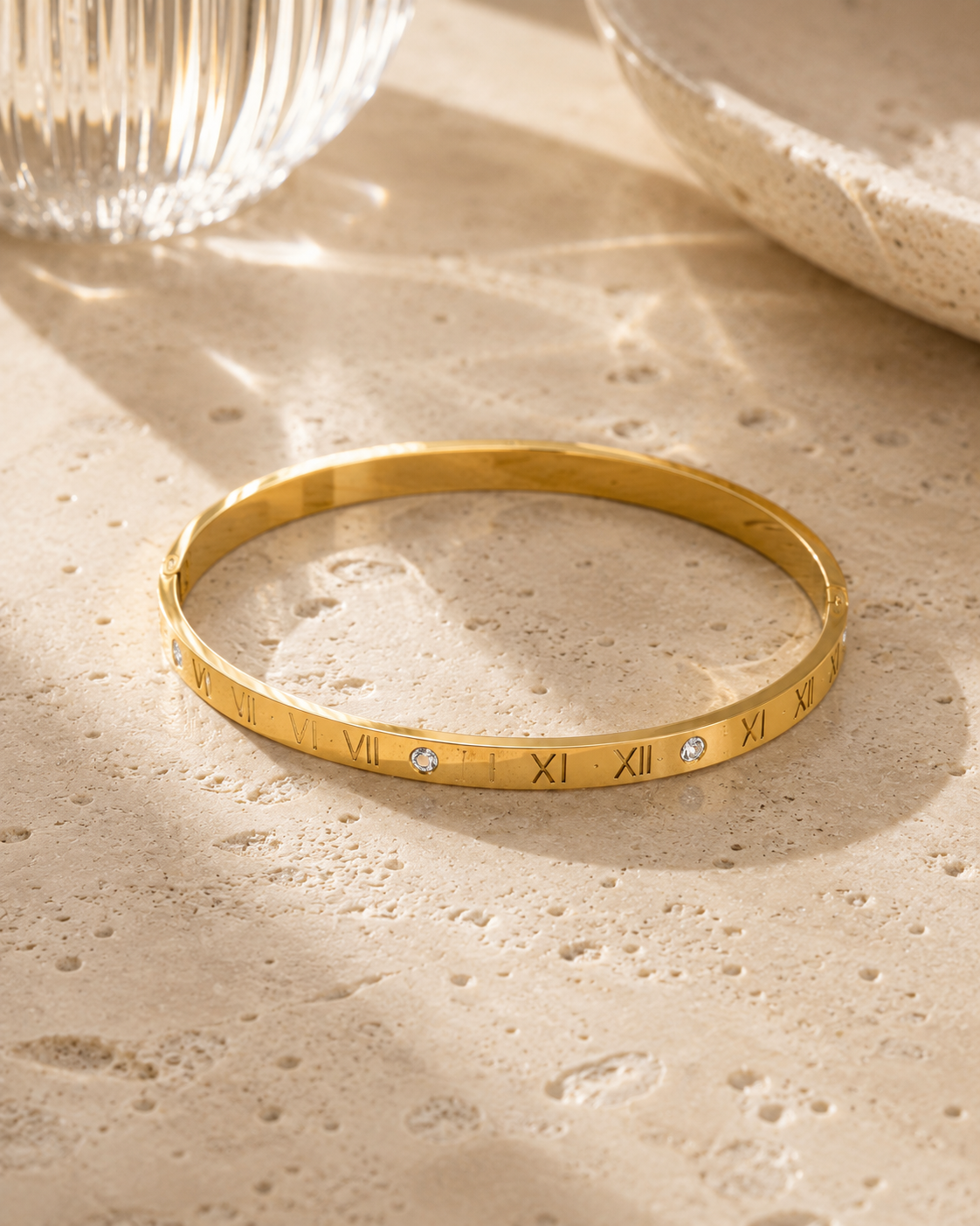 Goudkleurige armband met Romeinse cijfers en vier zirkonia stenen op luxe natuurstenen tafel.