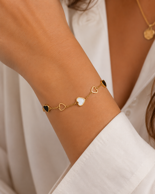 Model draagt gouden armband met zwarte en witte hartjes om de pols