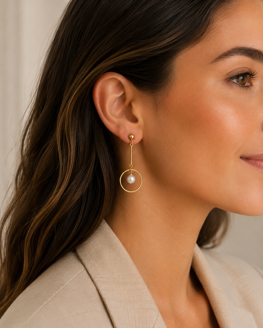 Model draagt gouden hangoorbellen met parel en ronde ring