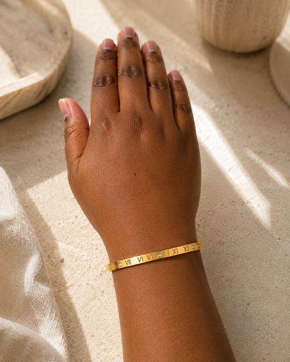 Model draagt goudkleurige armband met Romeinse cijfers en vier zirkonia stenen.