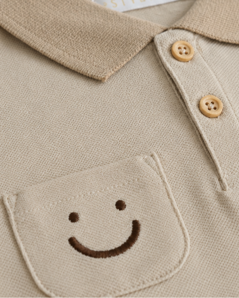 Close-up van beige baby polo met smiley borstzak, piqué stof en houten knoopjes