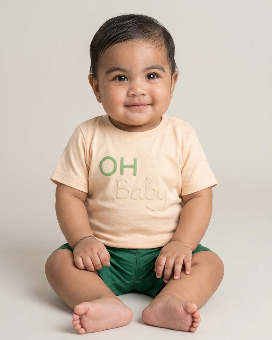 Lachende baby met beige OH Baby shirt en groene short, comfortabele baby outfit