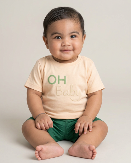 Lachende baby met beige OH Baby shirt en groene short, comfortabele baby outfit
